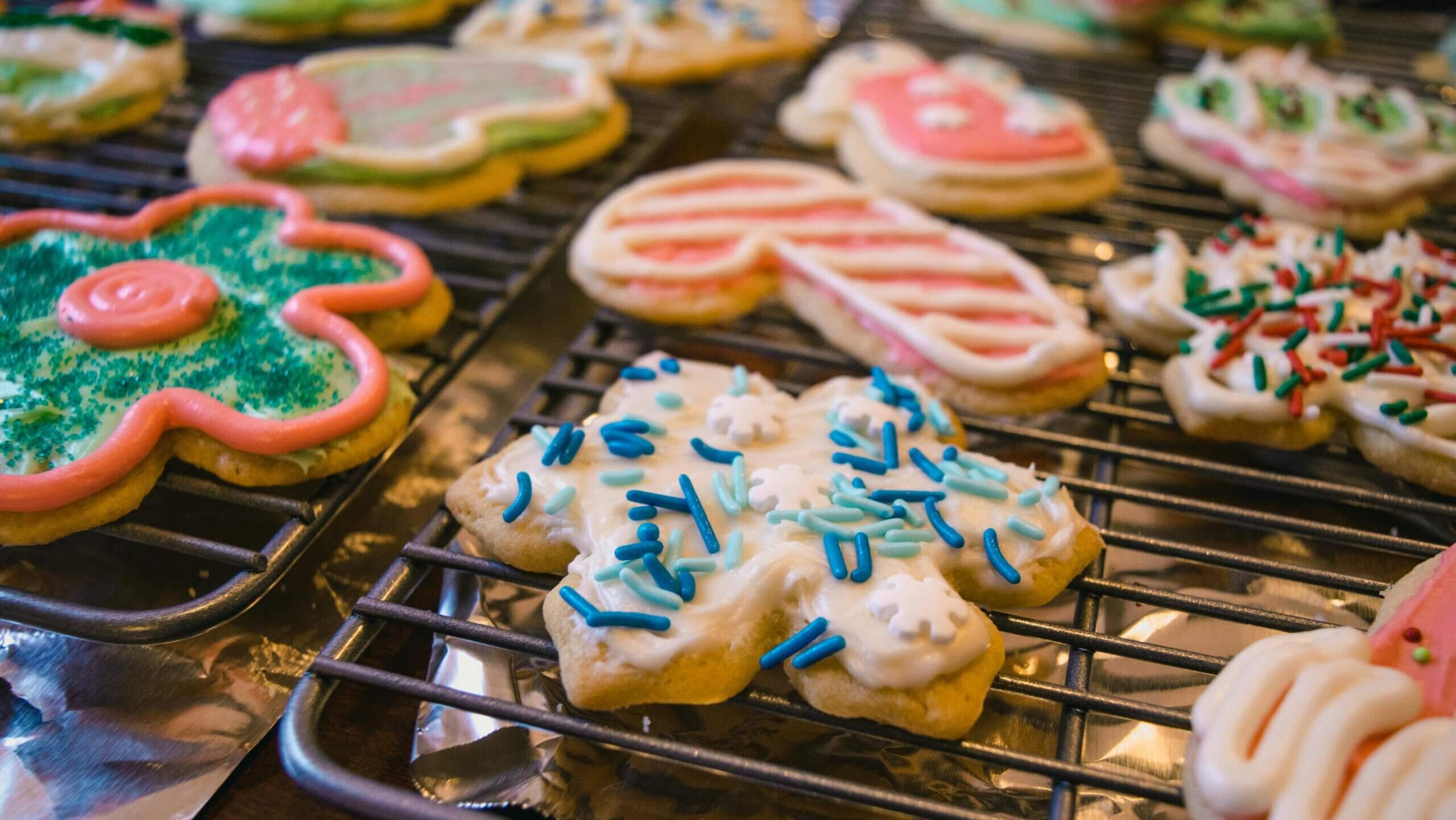 Assorted decorated Christmas sugar cookies cooling on wire racks with colorful icing and sprinkles.