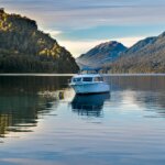 White motorboat anchored on calm lake surrounded by forested mountains at sunset