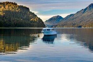 White motorboat anchored on calm lake surrounded by forested mountains at sunset