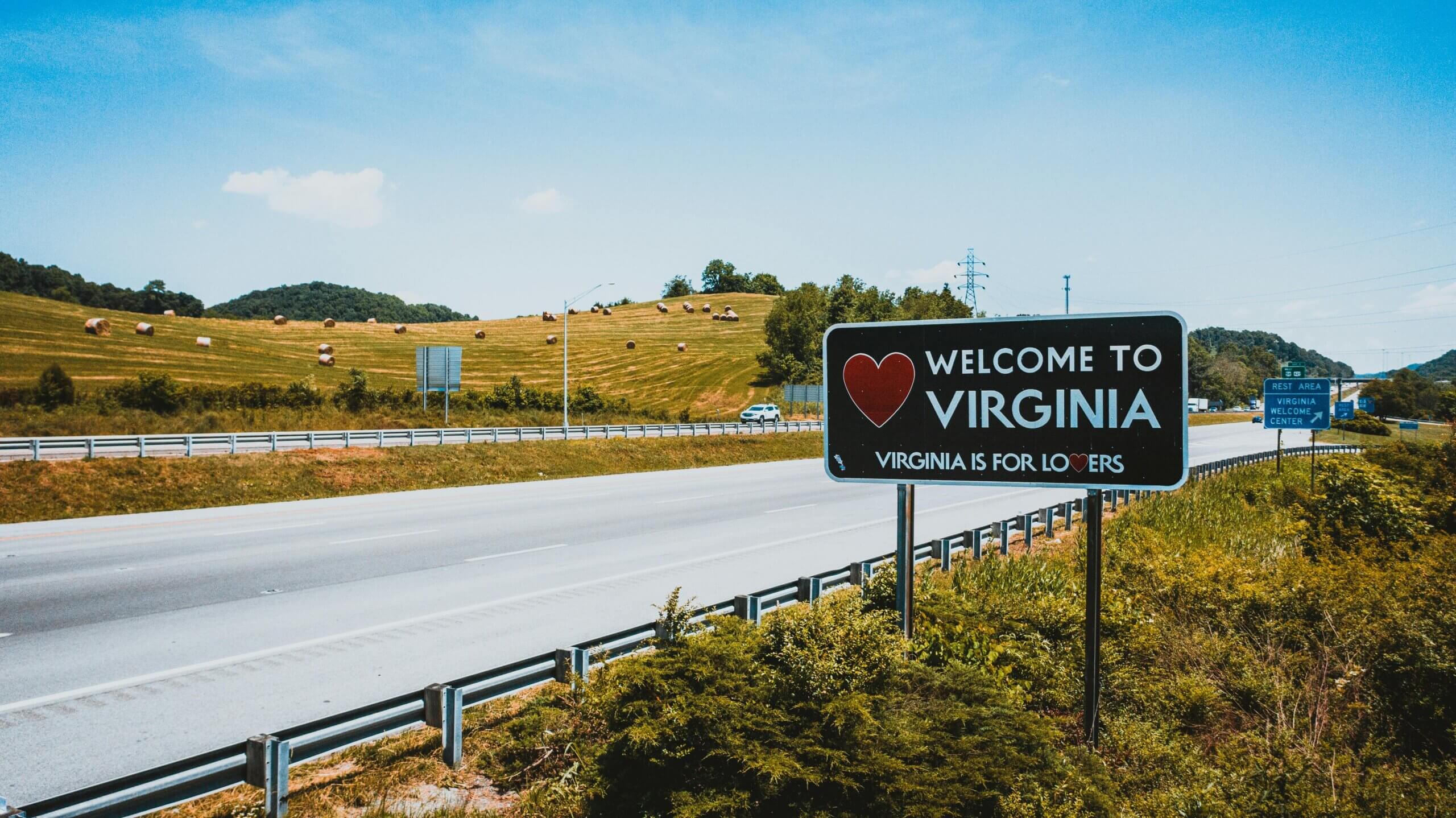 Welcome to Virginia road sign with "Virginia is for Lovers" slogan along a highway with hay bales in the background