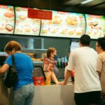 Customers ordering at a Jollibee fast food counter with menu boards displaying meals above.
