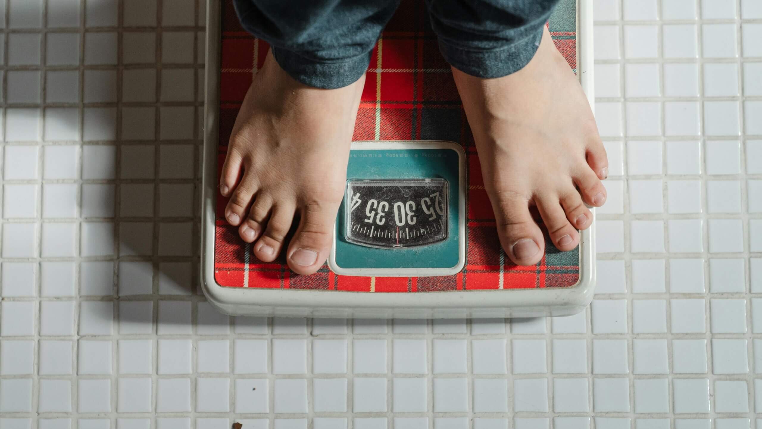 Bare feet standing on a red plaid analog bathroom scale showing a weight around 34 kilograms.