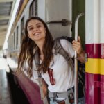 Smiling woman with backpack leaning out of a train door at a station platform.