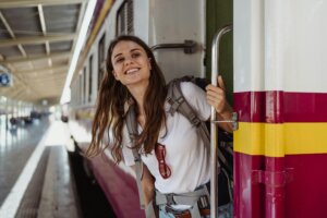 Smiling woman with backpack leaning out of a train door at a station platform.