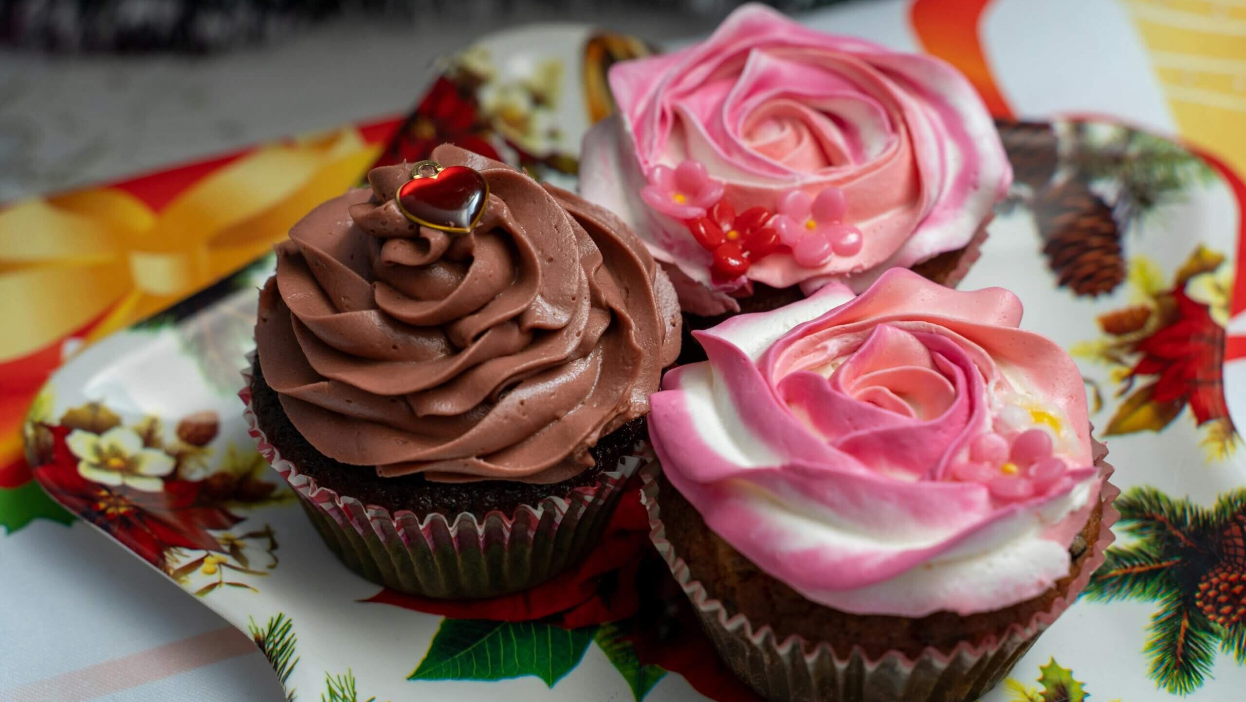 Three decorated cupcakes with chocolate and pink rose-shaped frosting on a festive holiday plate