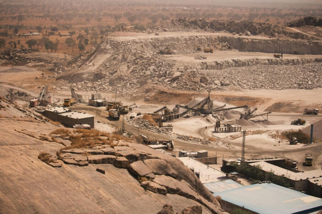 Open-pit quarry with heavy machinery and conveyor belts processing rocks in a dry, rocky landscape.