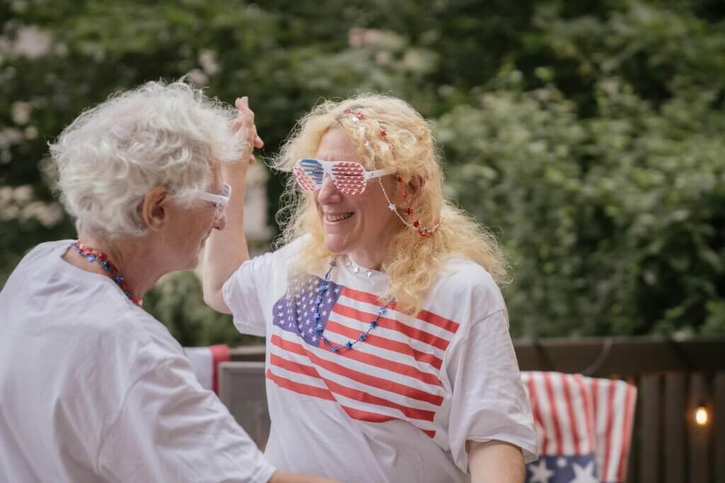 Two people wearing American flag-themed clothing and accessories smiling and dancing outdoors.