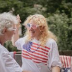 Two people wearing American flag-themed clothing and accessories smiling and dancing outdoors.