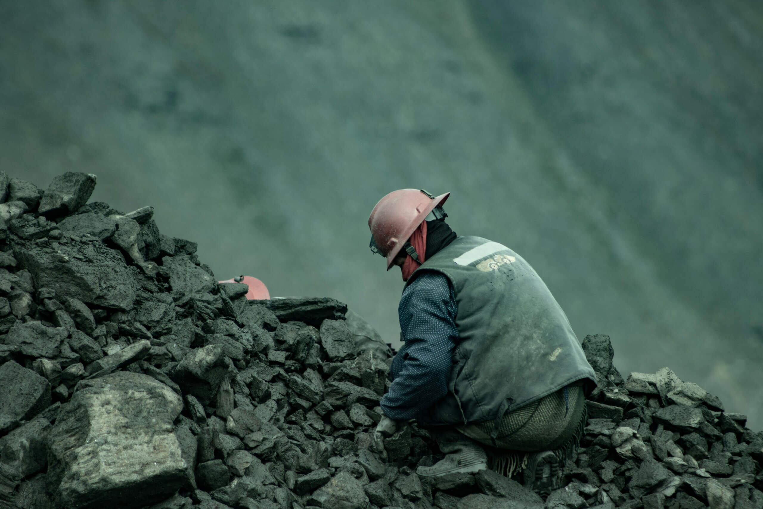 Miner wearing a red helmet and protective clothing working among coal rocks