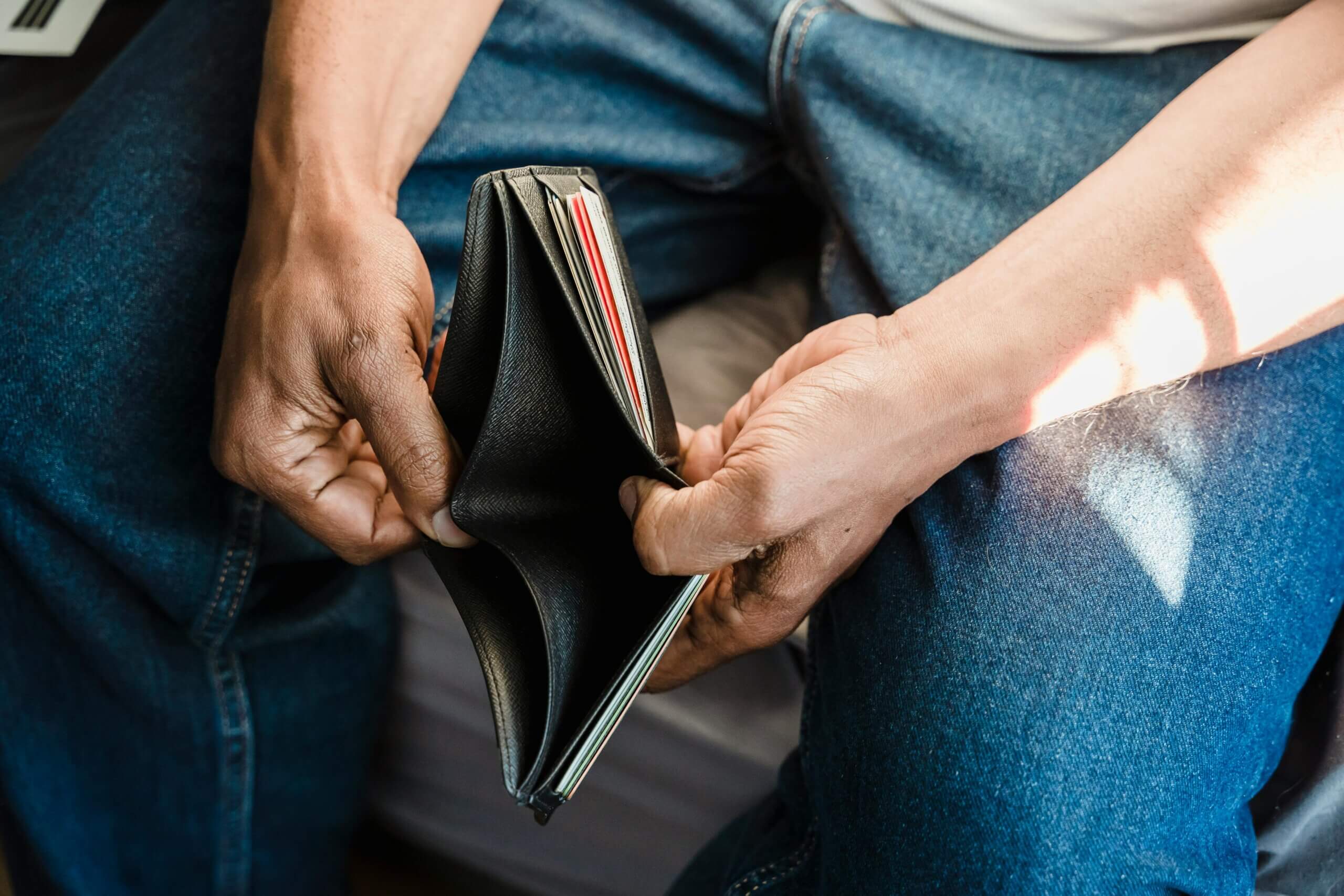 Two people holding an open black wallet showing empty compartments and some cards inside.