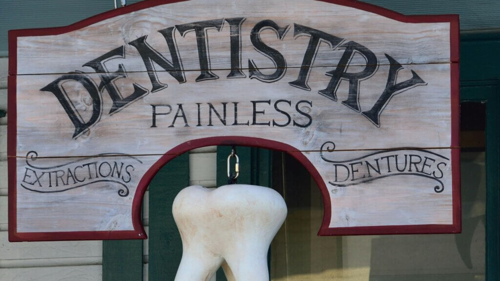 Wooden dentistry sign with "Painless," "Extractions," and "Dentures" text and a large hanging tooth model