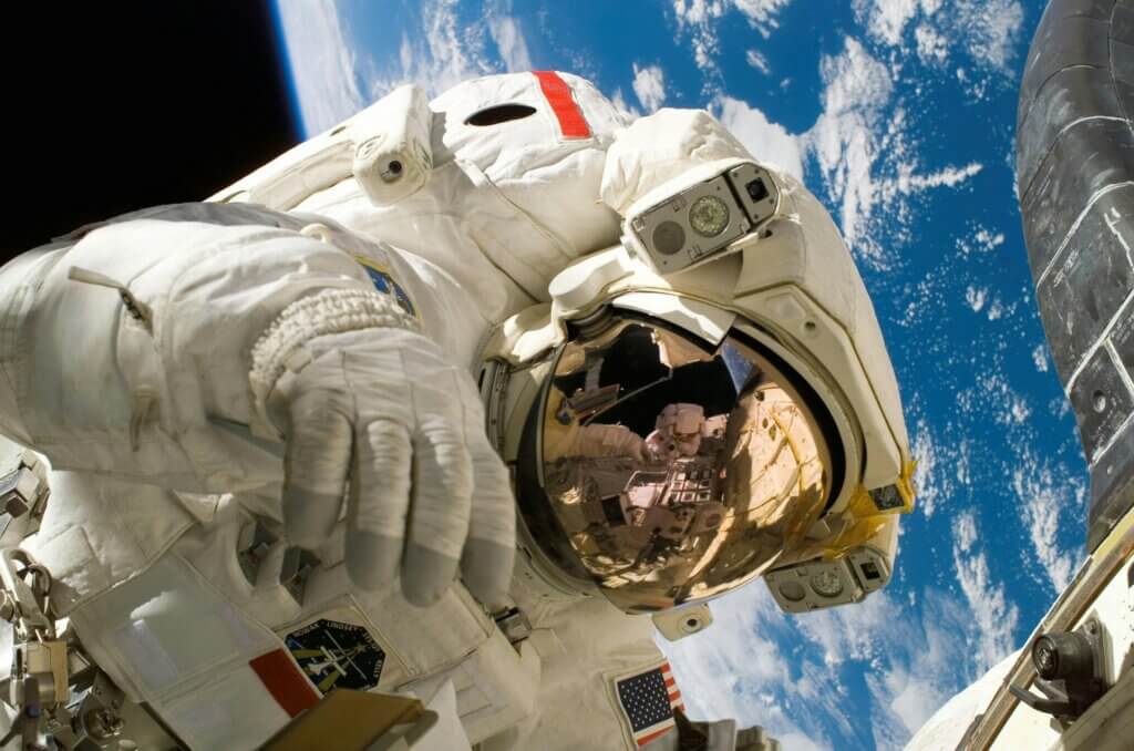Astronaut in a white spacesuit performing a spacewalk with Earth and a spacecraft in the background.