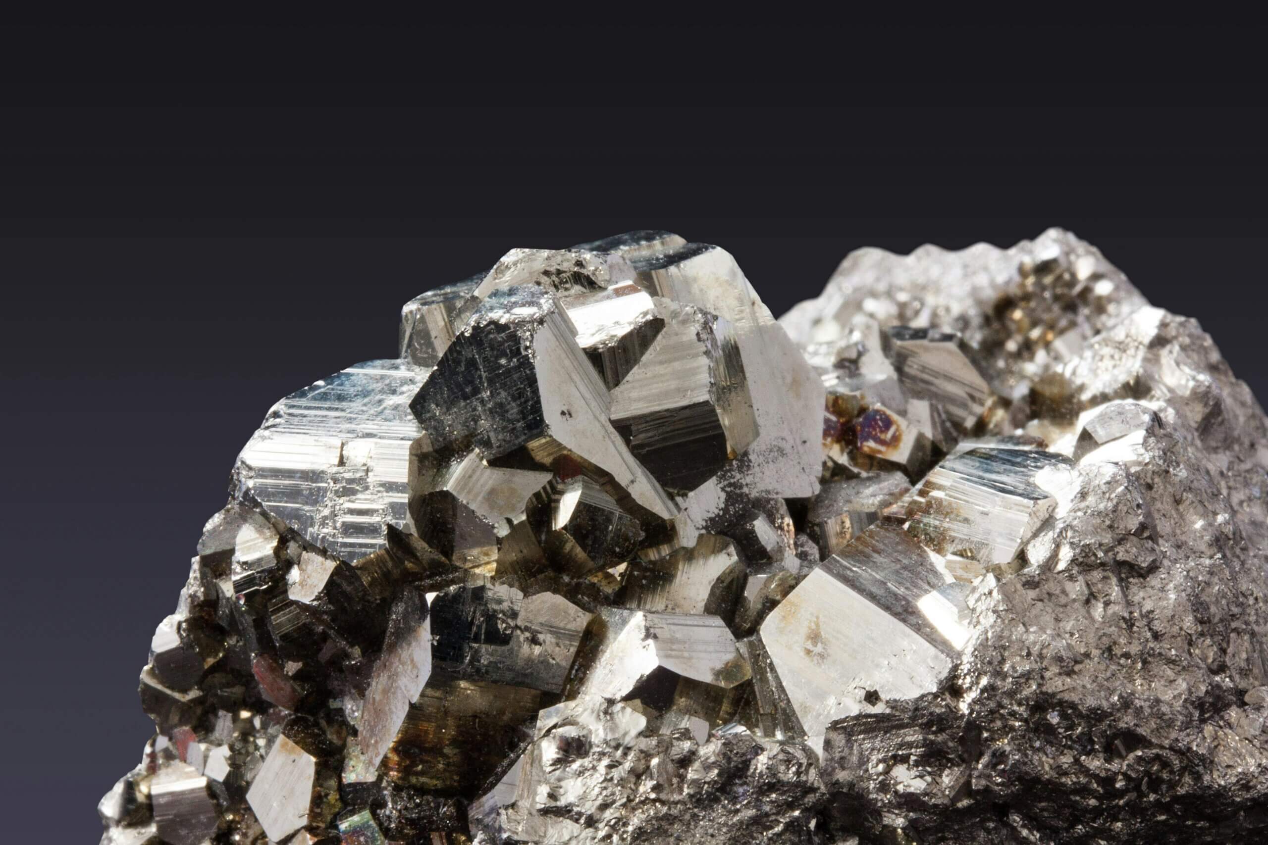 Close-up of shiny metallic pyrite crystals on a rough rock matrix against a dark background