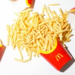 Three empty McDonald's red fry containers with spilled French fries on a white surface
