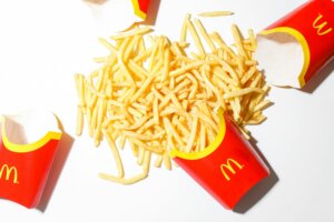 Three empty McDonald's red fry containers with spilled French fries on a white surface