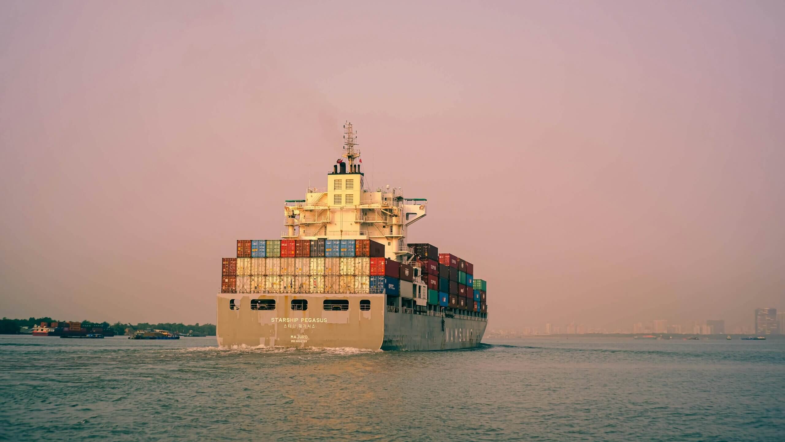 Cargo ship Starship Pegasus loaded with containers sailing on calm water at sunset