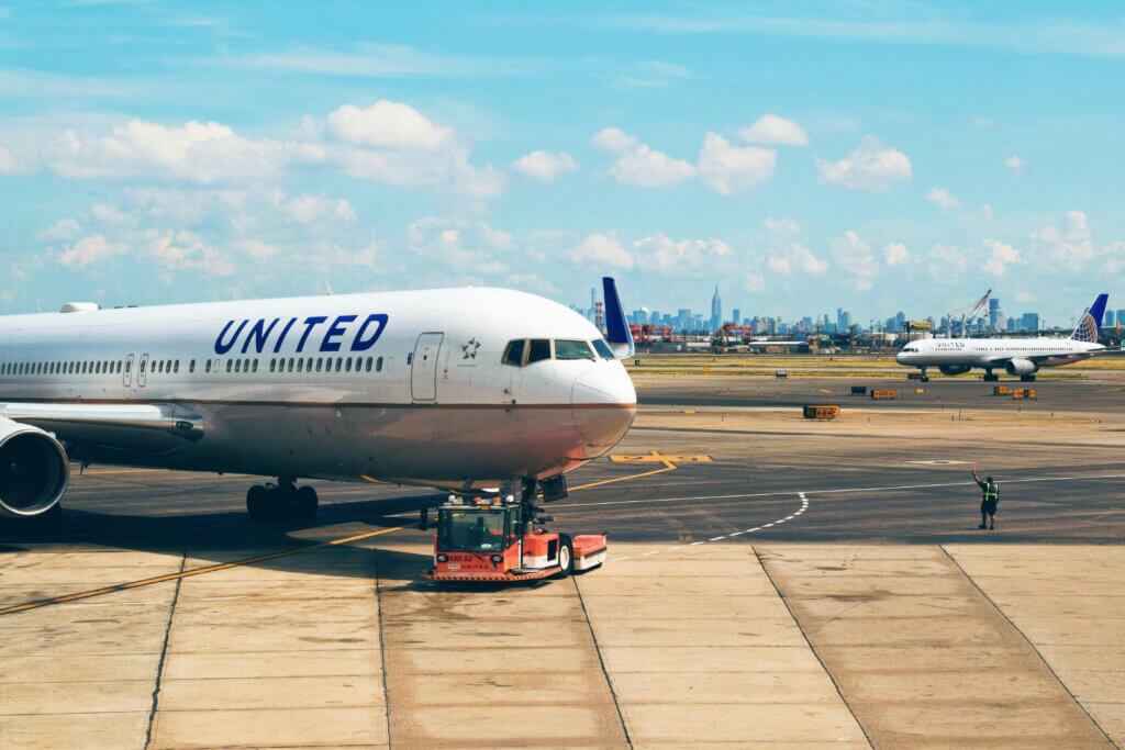 United Airlines planes on the tarmac with a ground crew member directing near a city skyline under a blue sky