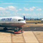 United Airlines planes on the tarmac with a ground crew member directing near a city skyline under a blue sky