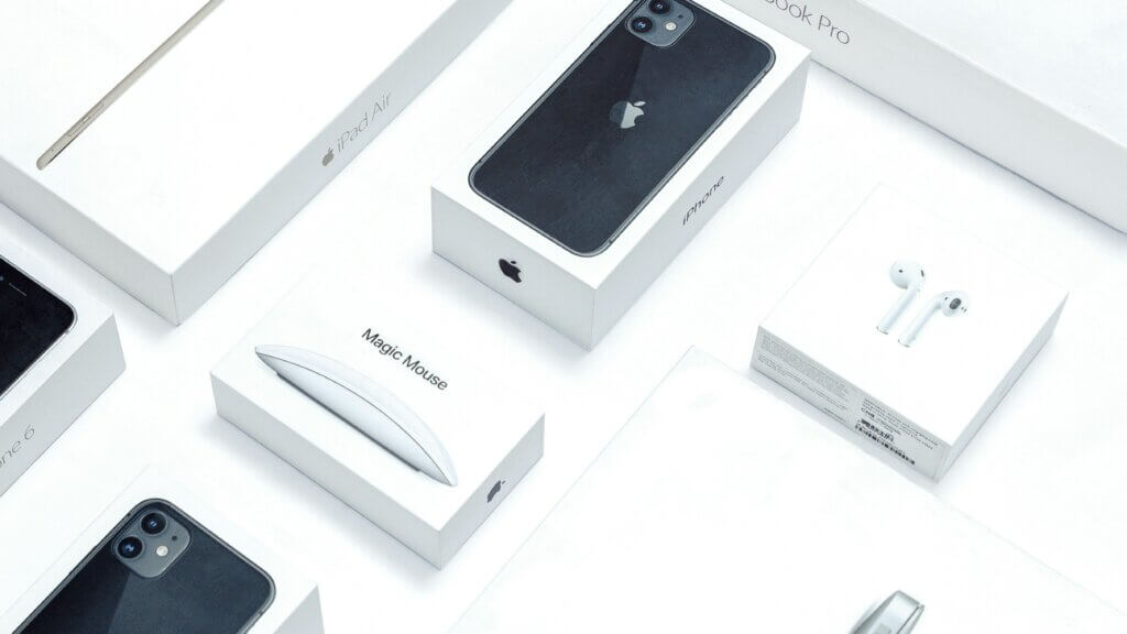 Apple product boxes including iPhone, iPad Air, Magic Mouse, AirPods, and MacBook Pro on a white surface