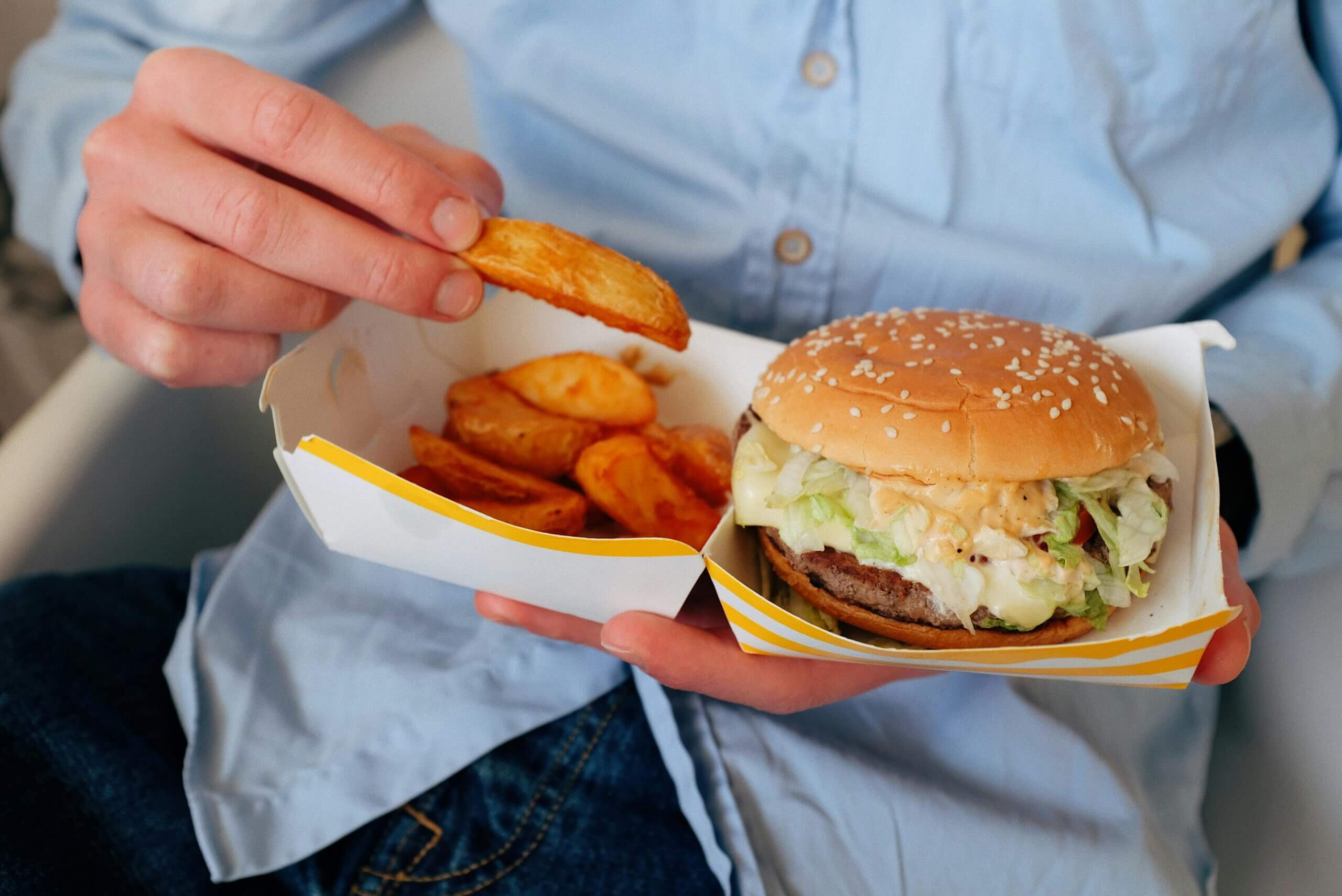 Person holding a fast food meal with a cheeseburger and potato wedges in a white and yellow container