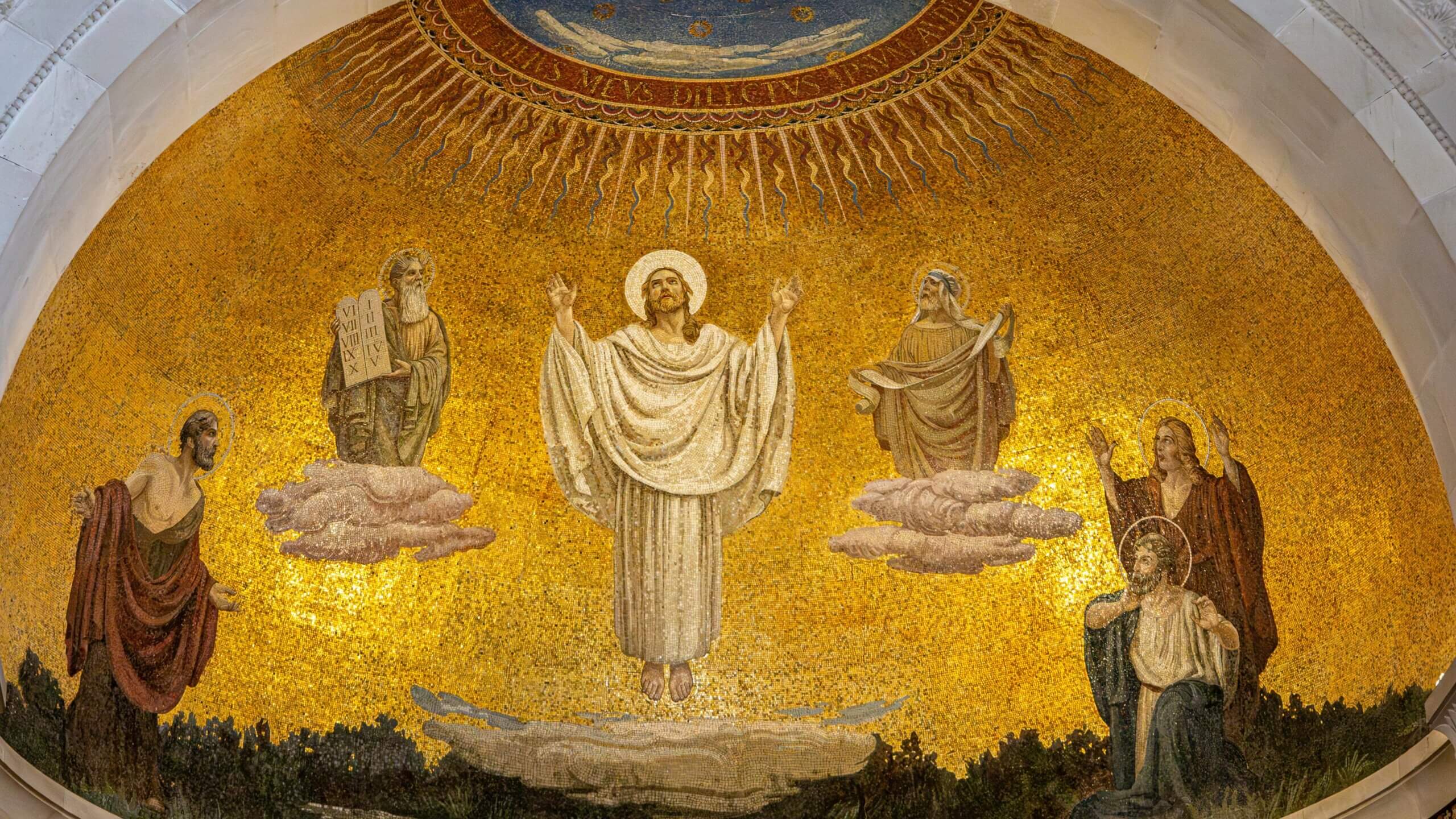 Mosaic of Jesus Christ in white robe with halo, flanked by biblical figures on golden background in church apse.