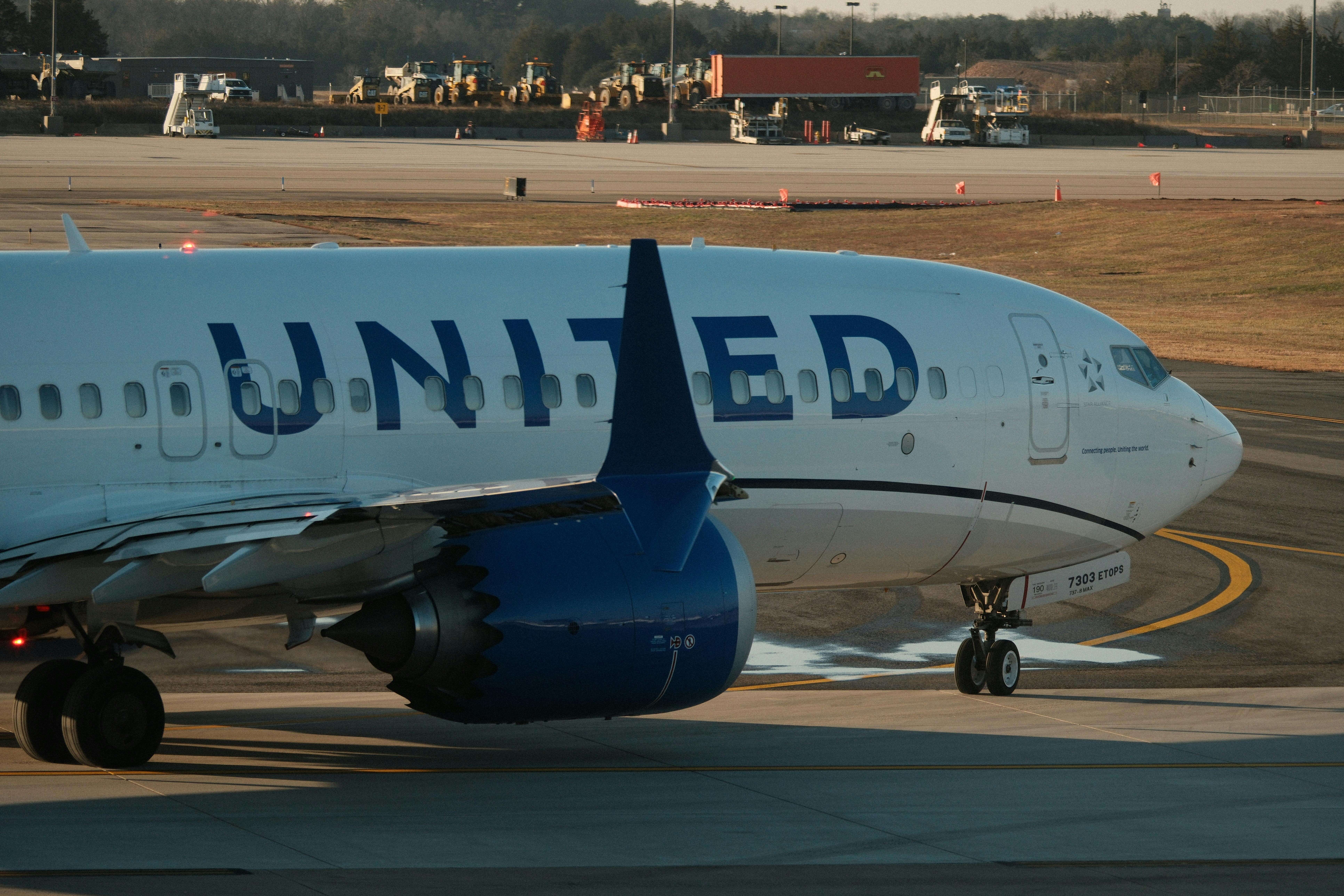 United Airlines airplane taxiing on airport runway with ground service vehicles in background