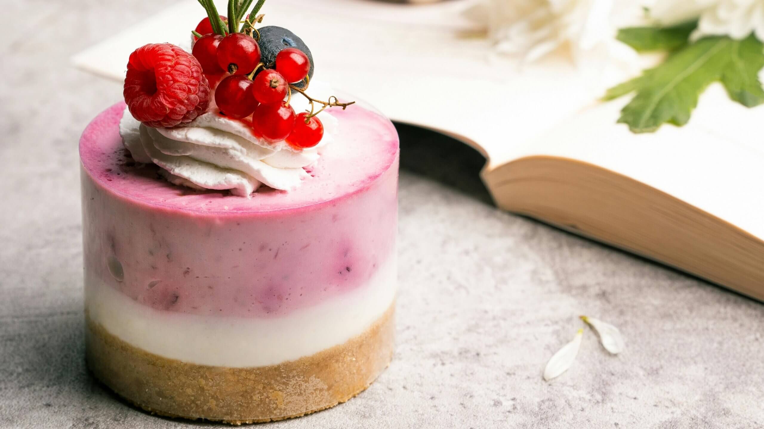 Mini layered berry cheesecake with whipped cream and fresh berries on top next to an open book