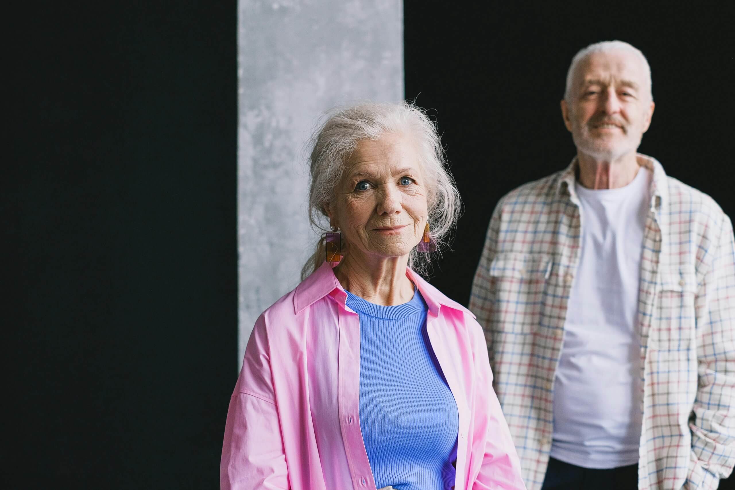 Older woman in a pink shirt and blue top with an older man in a plaid shirt and white t-shirt behind her