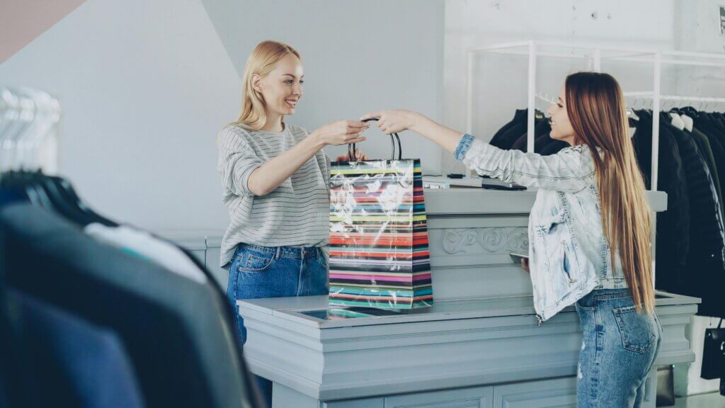 Customer receiving a striped shopping bag from a cashier at a clothing store counter