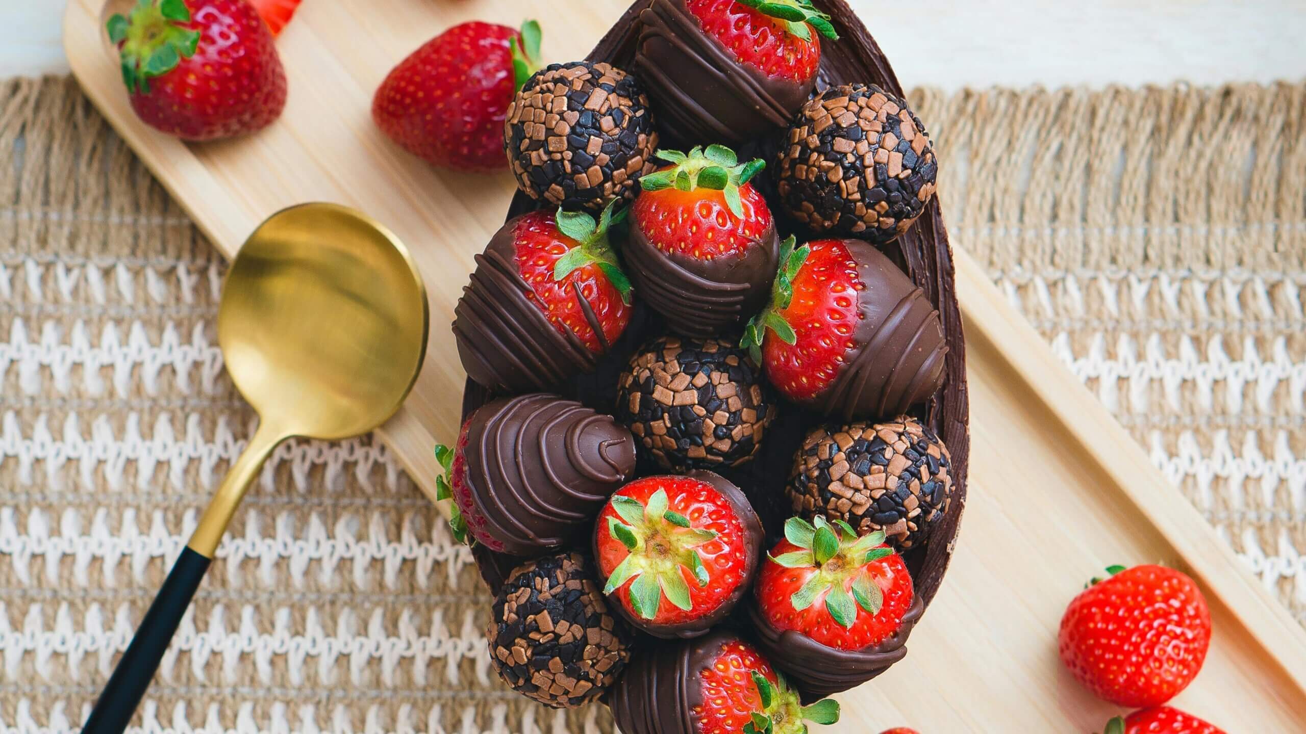 Chocolate-covered strawberries and chocolate truffles arranged in a chocolate bowl on a wooden tray with a gold spoon.