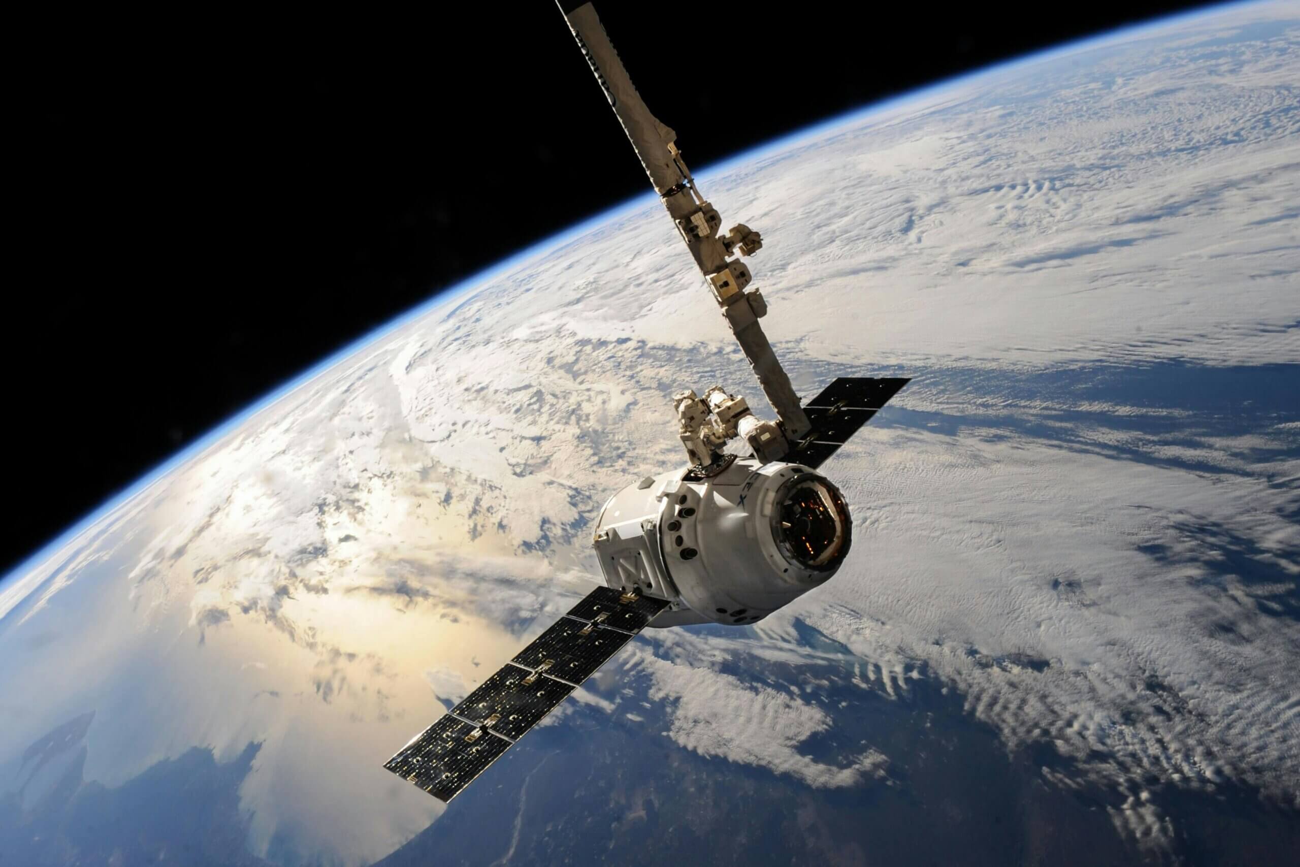 SpaceX Dragon spacecraft with solar panels orbiting Earth above cloud cover.