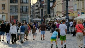 Crowd of people walking on a cobblestone street near Bank Pekao in a European city center.