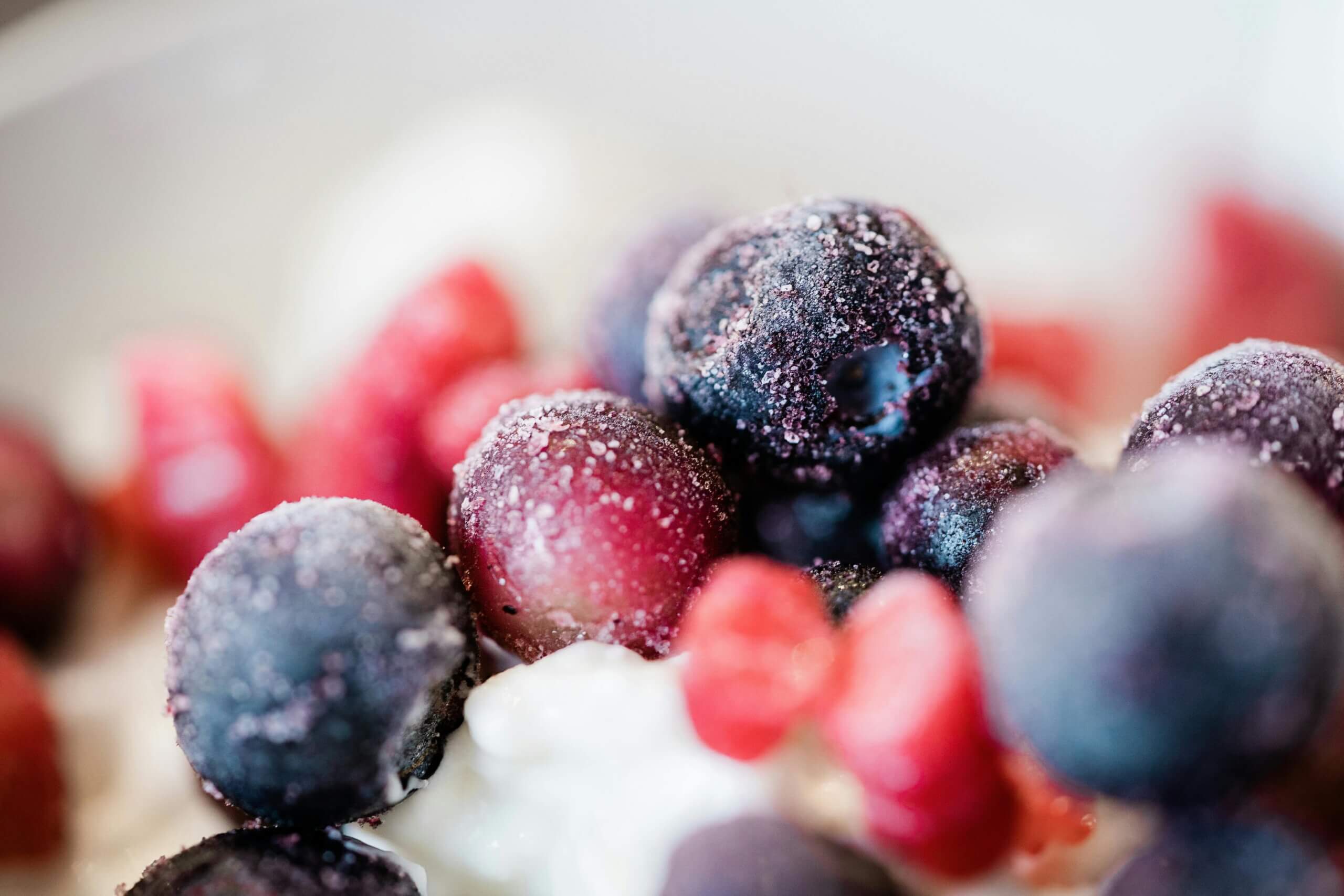 Close-up of frozen blueberries and raspberries on creamy yogurt.