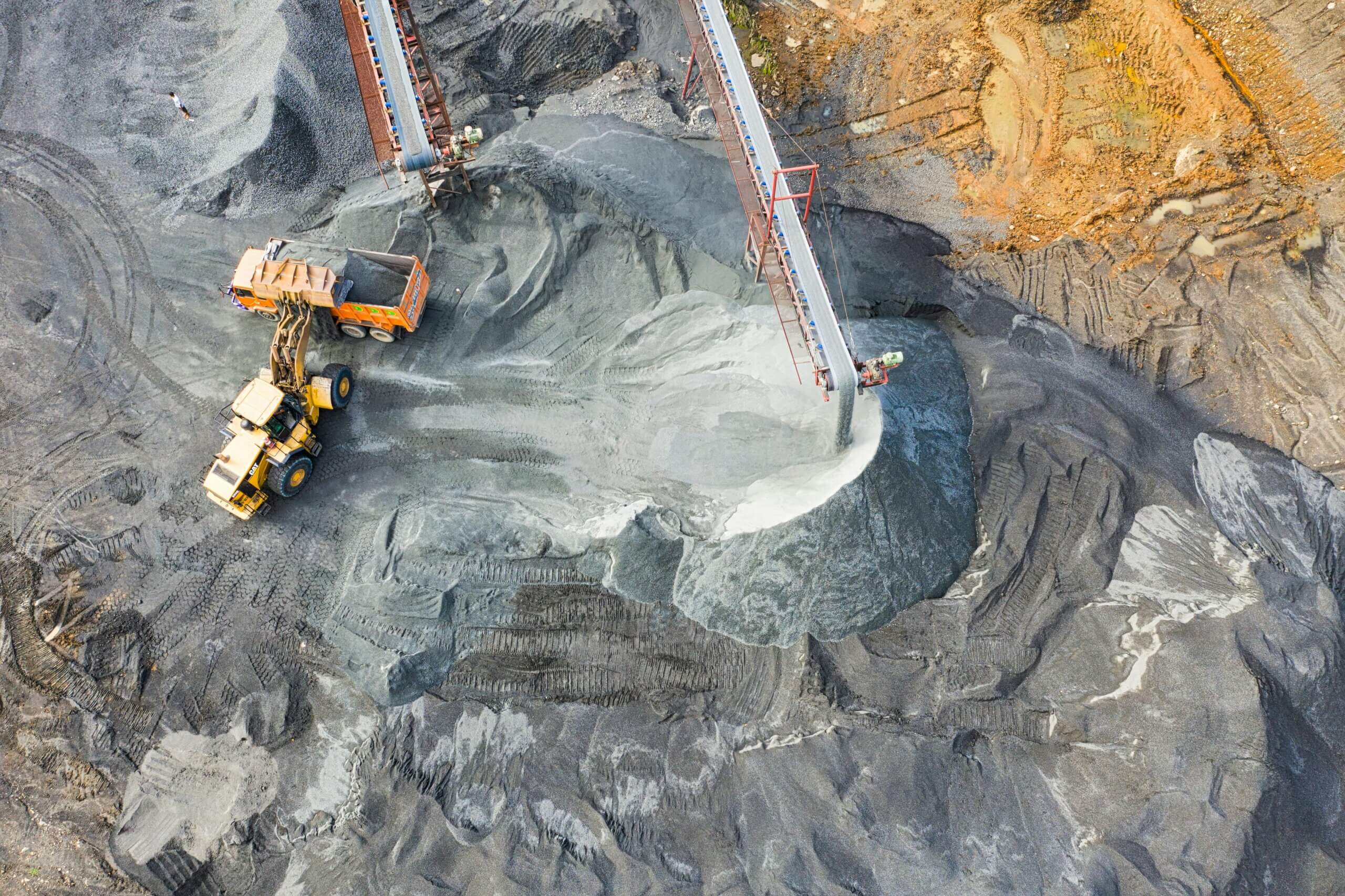 Aerial view of a yellow loader dumping gravel into an orange dump truck at a quarry site.