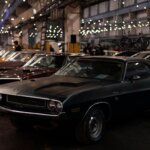 Black Dodge Challenger R/T parked indoors with other vintage cars and string lights overhead