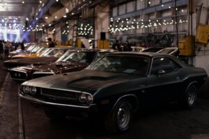 Black Dodge Challenger R/T parked indoors with other vintage cars and string lights overhead