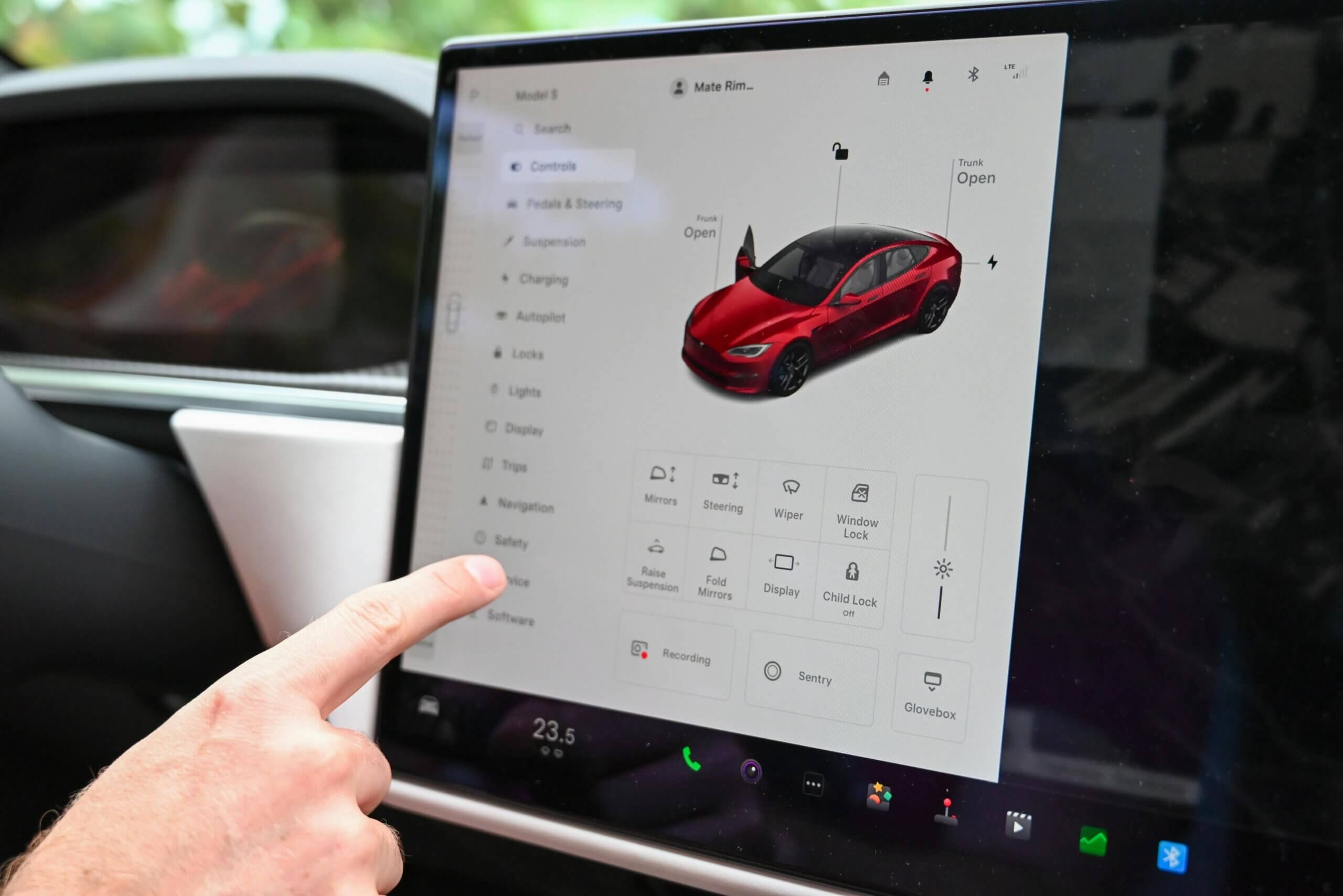 Finger pointing at Tesla Model S touchscreen displaying car controls with open frunk and trunk icons