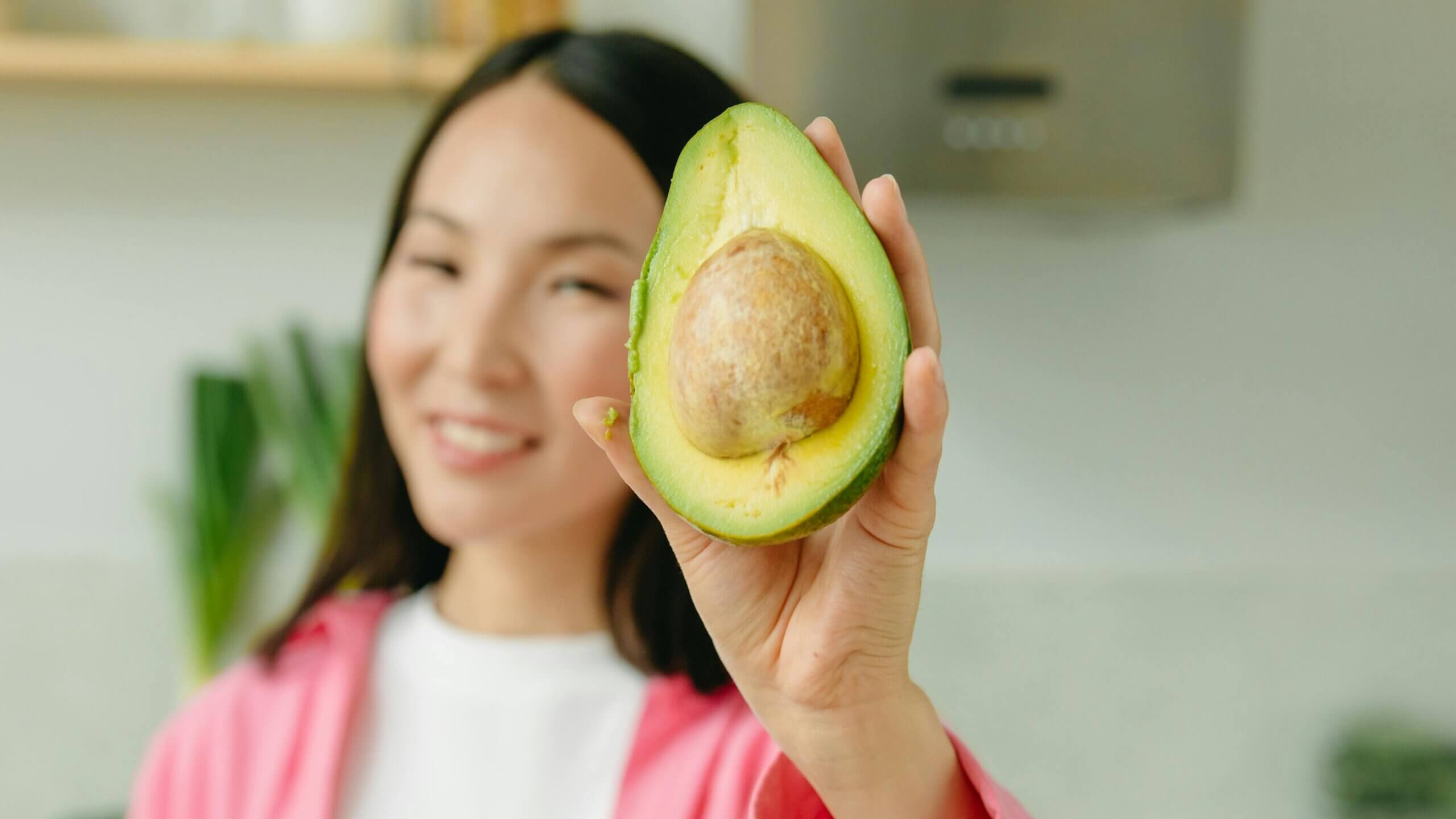 Woman holding a halved avocado with the pit visible in a kitchen setting