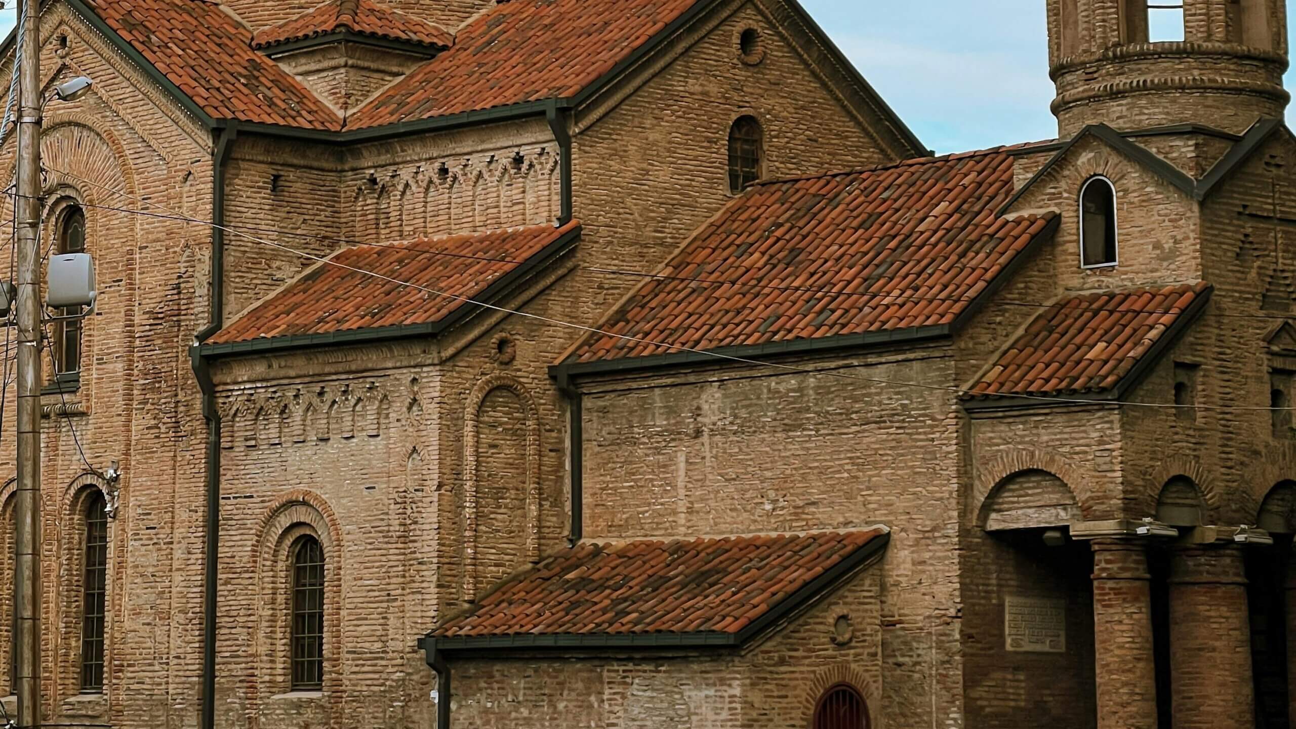 Historic brick church with red tiled roofs and arched windows under a clear sky