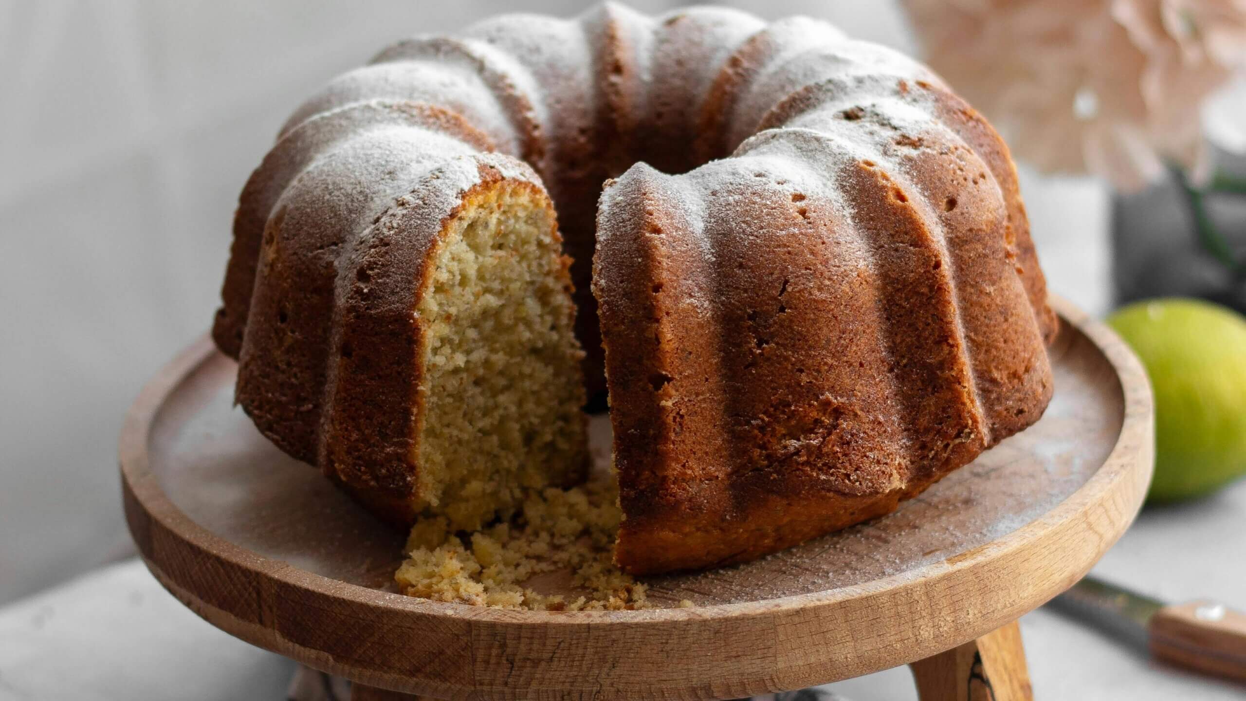 Bundt cake dusted with powdered sugar on a wooden cake stand with a slice removed
