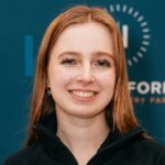 Smiling red-haired woman wearing a black zip-up jacket in front of a blue background with "Fork" text.