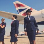 British Airways pilots and flight attendants walking on the tarmac near a British Airways airplane tailfin