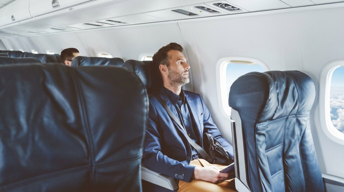 Man in blue blazer sitting by airplane window holding phone and looking outside during flight