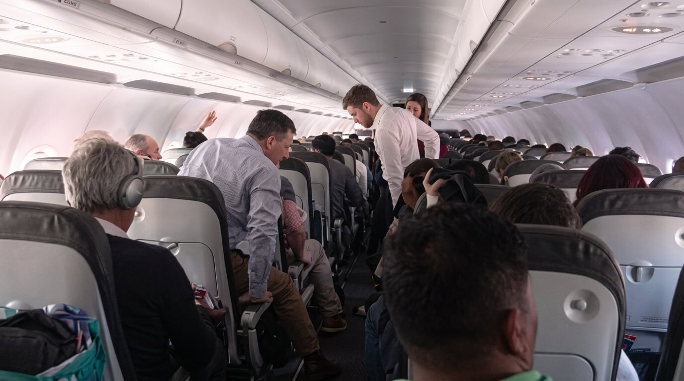 Passengers seated and standing in the aisle inside a commercial airplane cabin.