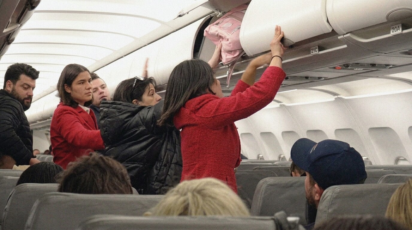 Passengers storing luggage in overhead bins inside an airplane cabin during boarding