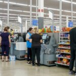 Customers and a Walmart employee using self-checkout stations near candy displays and fitting rooms.