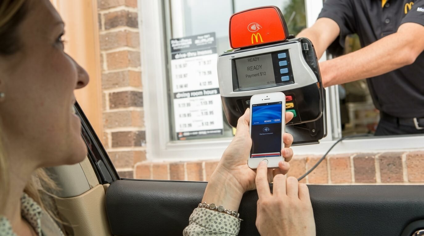 Woman using mobile phone to make a $12 contactless payment at a McDonald's drive-thru window terminal