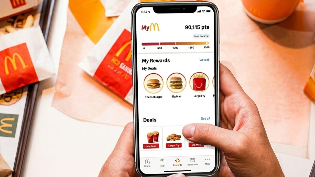 Hand holding iPhone displaying McDonald's app rewards with cheeseburger, Big Mac, and large fry deals visible