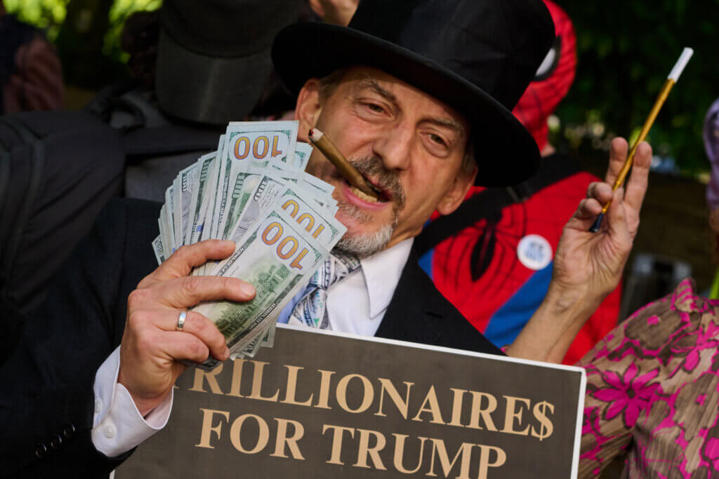Man in top hat holding cigar, fan of $100 bills, and sign reading "Billionaires for Trump"