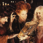 The Sanderson sisters from Hocus Pocus excitedly holding the magical spellbook by candlelight